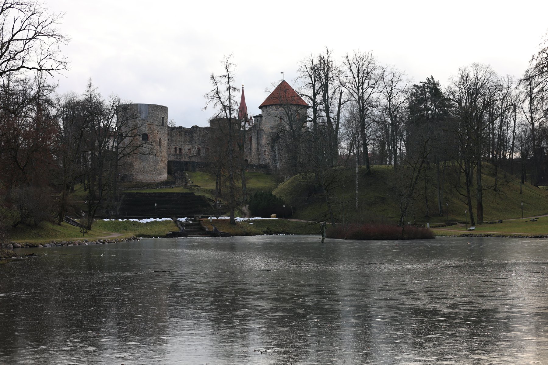 Castillo de Cēsis reflejado en un estanque invernal con árboles desnudos