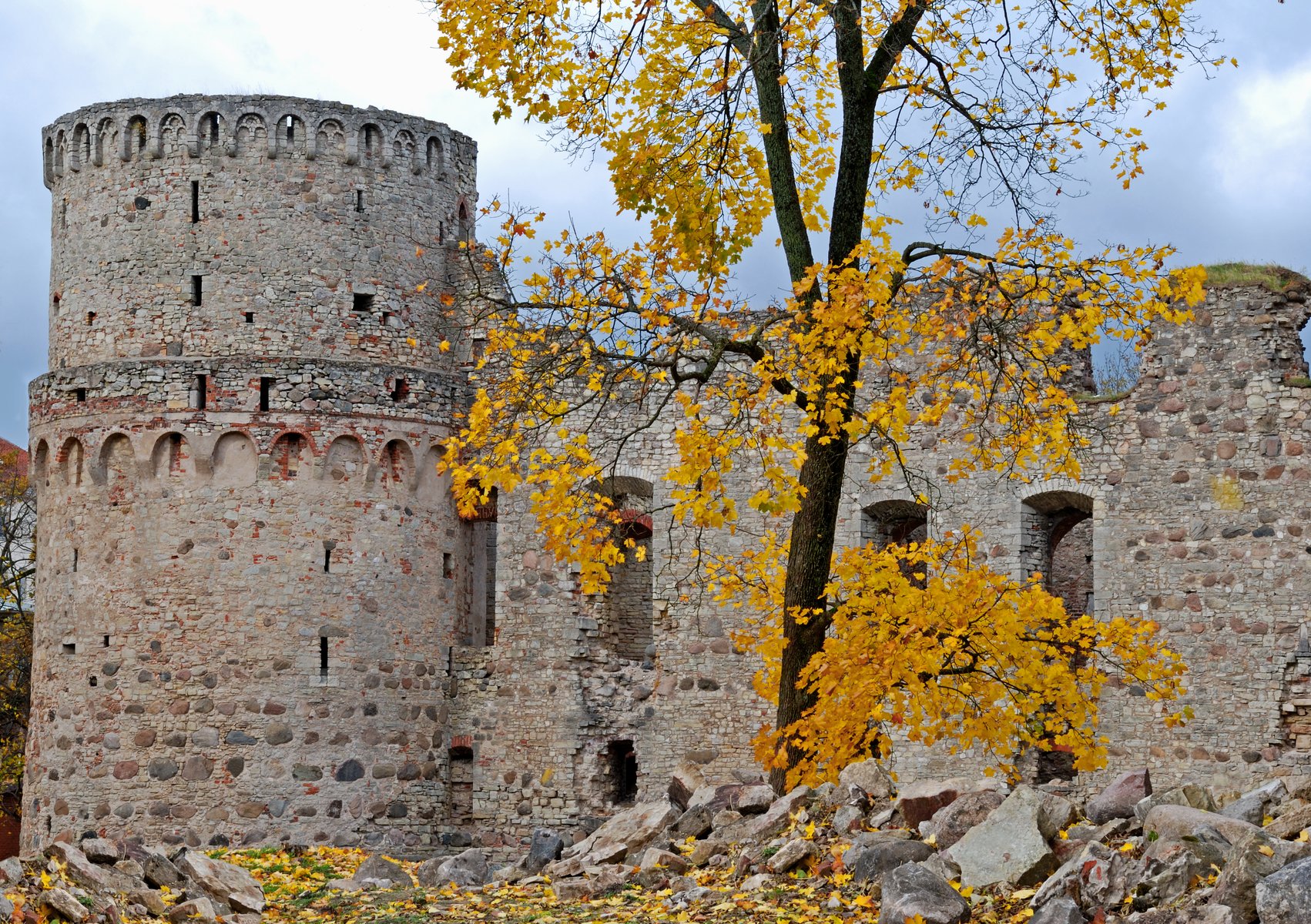 Muros de piedra del castillo de Cēsis enmarcados por hojas doradas de otoño