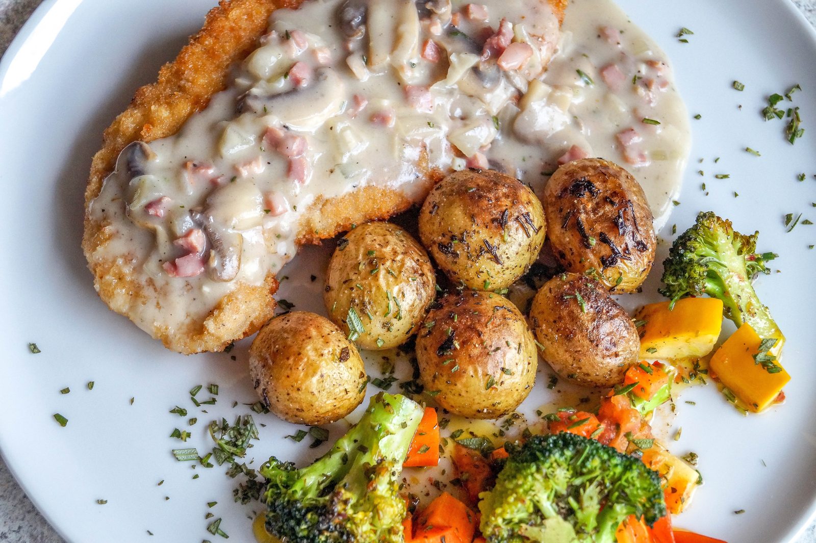 Plato de karbonāde &mdash; chuleta empanada letona &mdash; con salsa cremosa de setas, patatas con hierbas y verduras asadas
