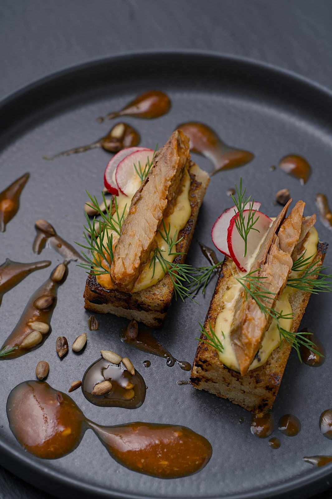 Aperitivo de pescado ahumado sobre tostada de centeno con crema, eneldo y rabanito, en un plato negro
