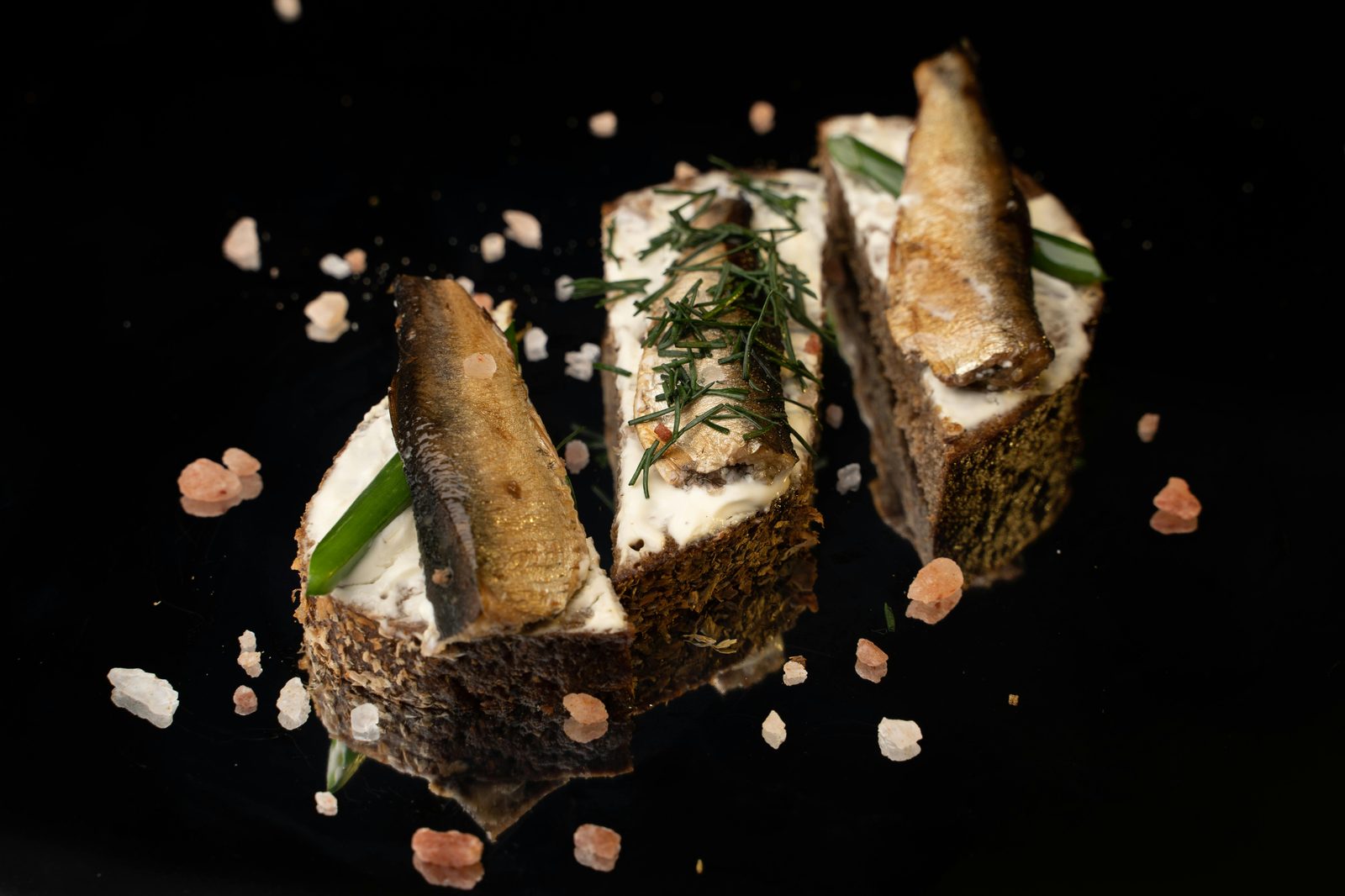 Tres espadines ahumados sobre pan de centeno con nata agria y eneldo, sobre fondo negro
